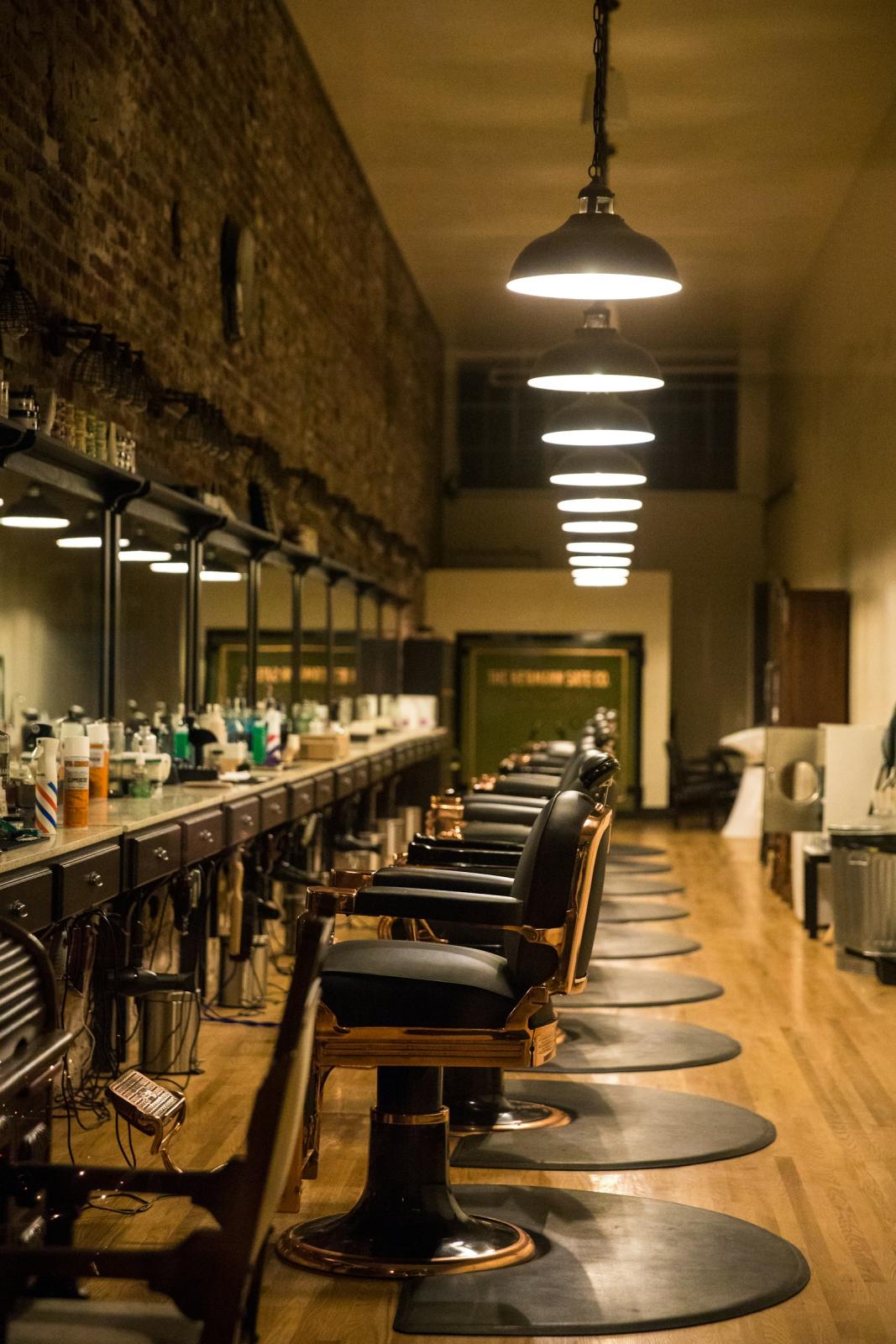 A long row of leather barber chairs under pendant lights